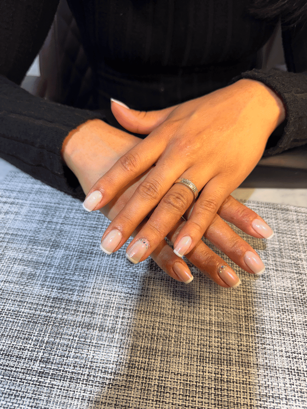 Manicured hands with rings resting on a textured surface.