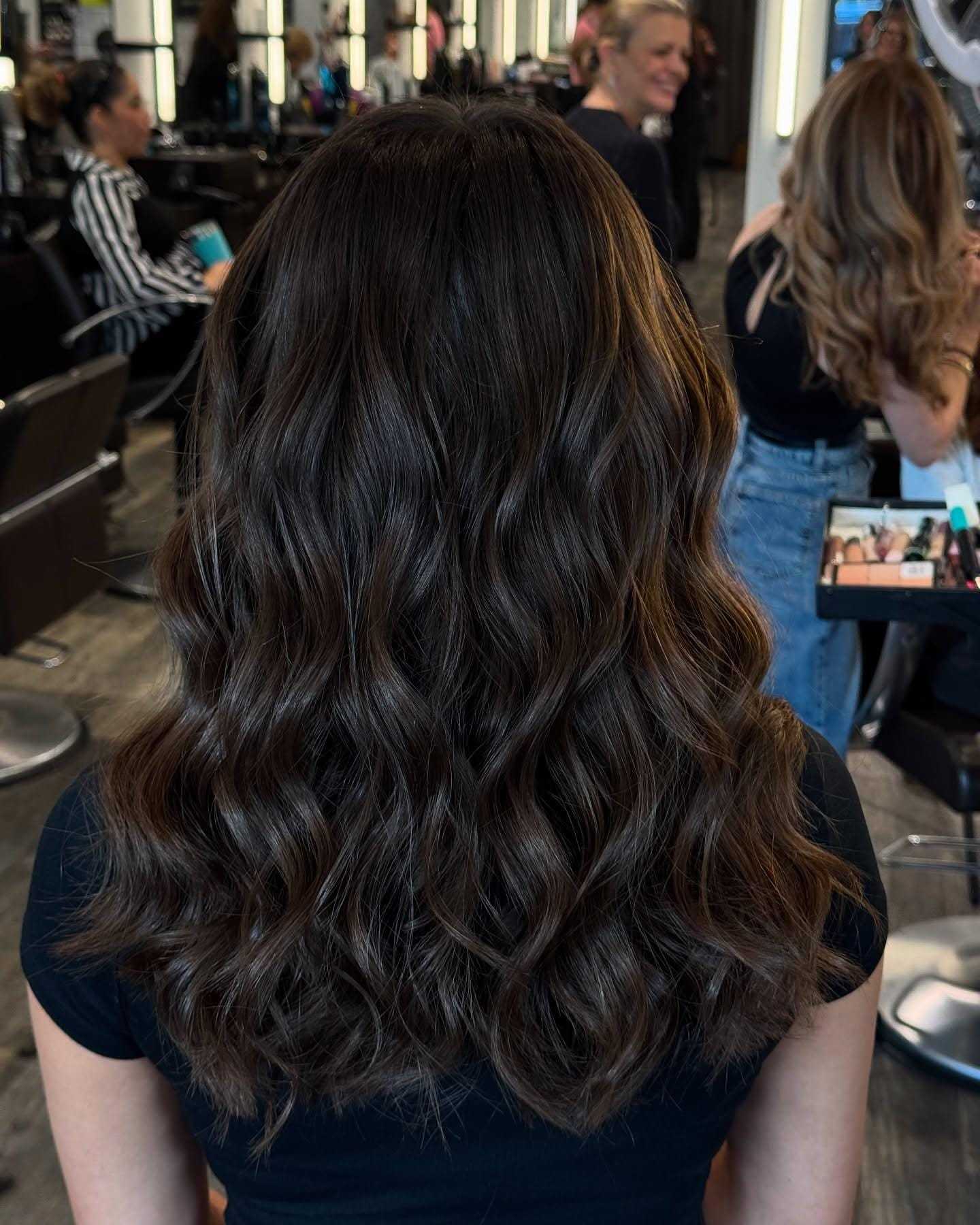Wavy brown hair styled at a busy salon, viewed from behind.