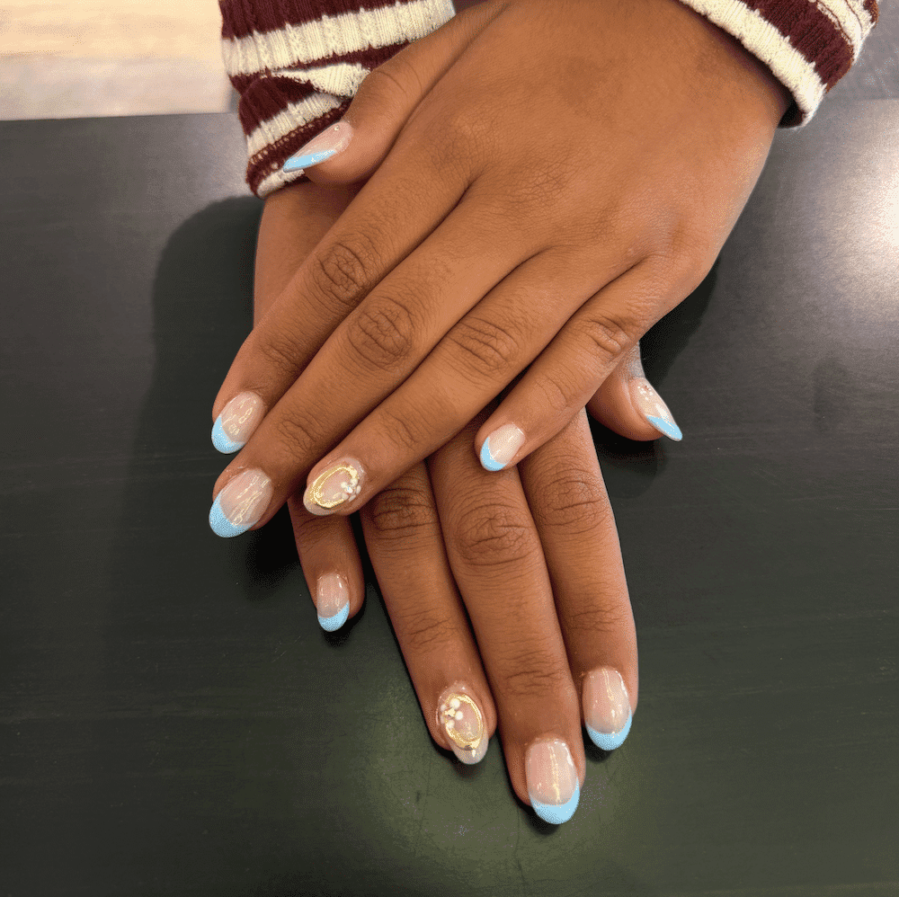 Nails with blue French tips and decorative accents on dark table.