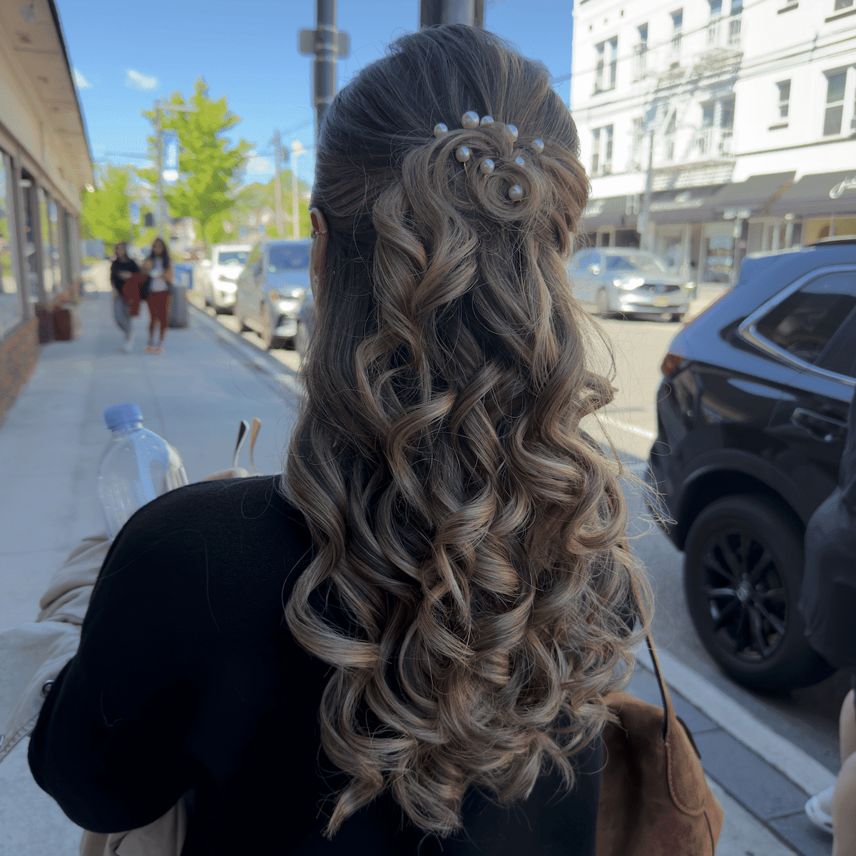 Hair with loose curls and pearl accessory, walking on a sunny sidewalk.