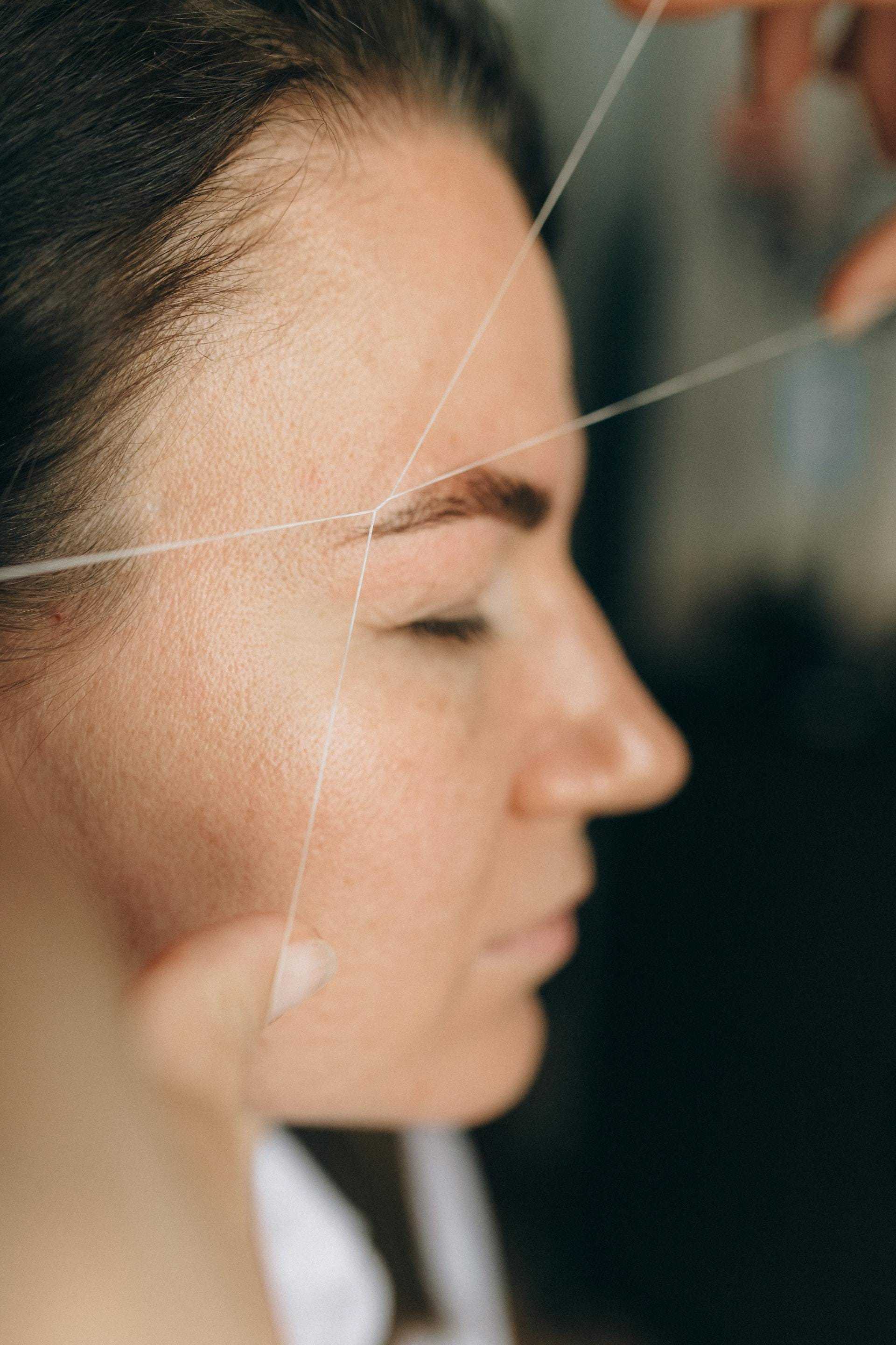 Eyebrow threading in progress on a woman's face.