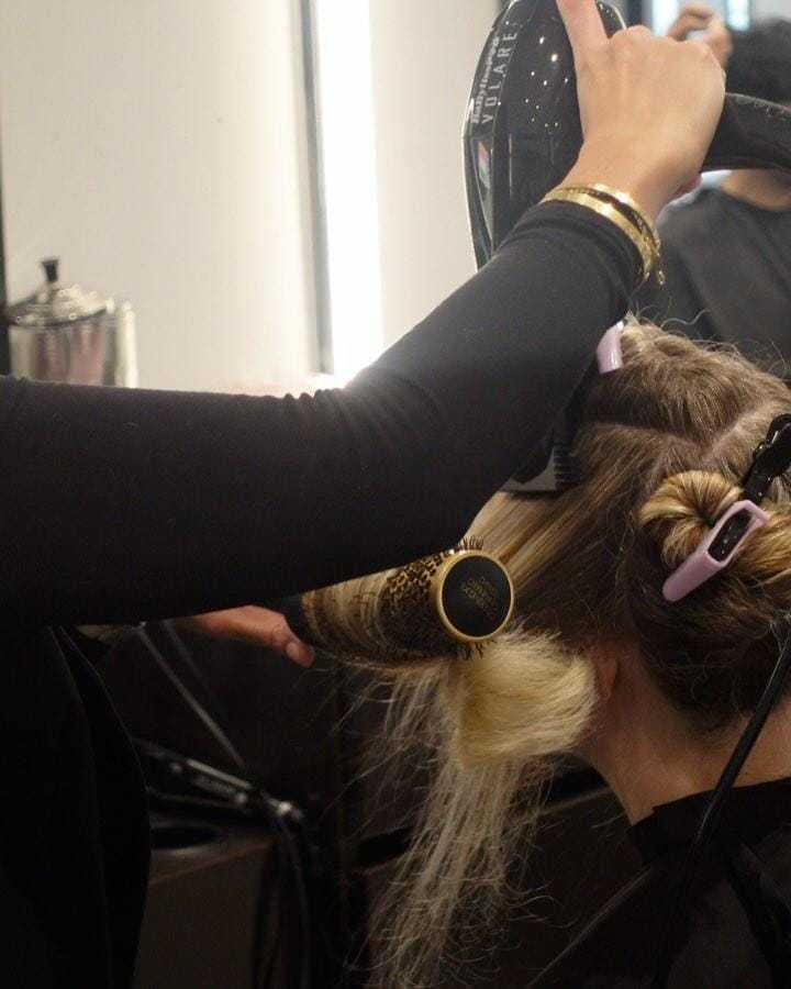 Hair stylist blow-drying client's hair with brush in salon setting.