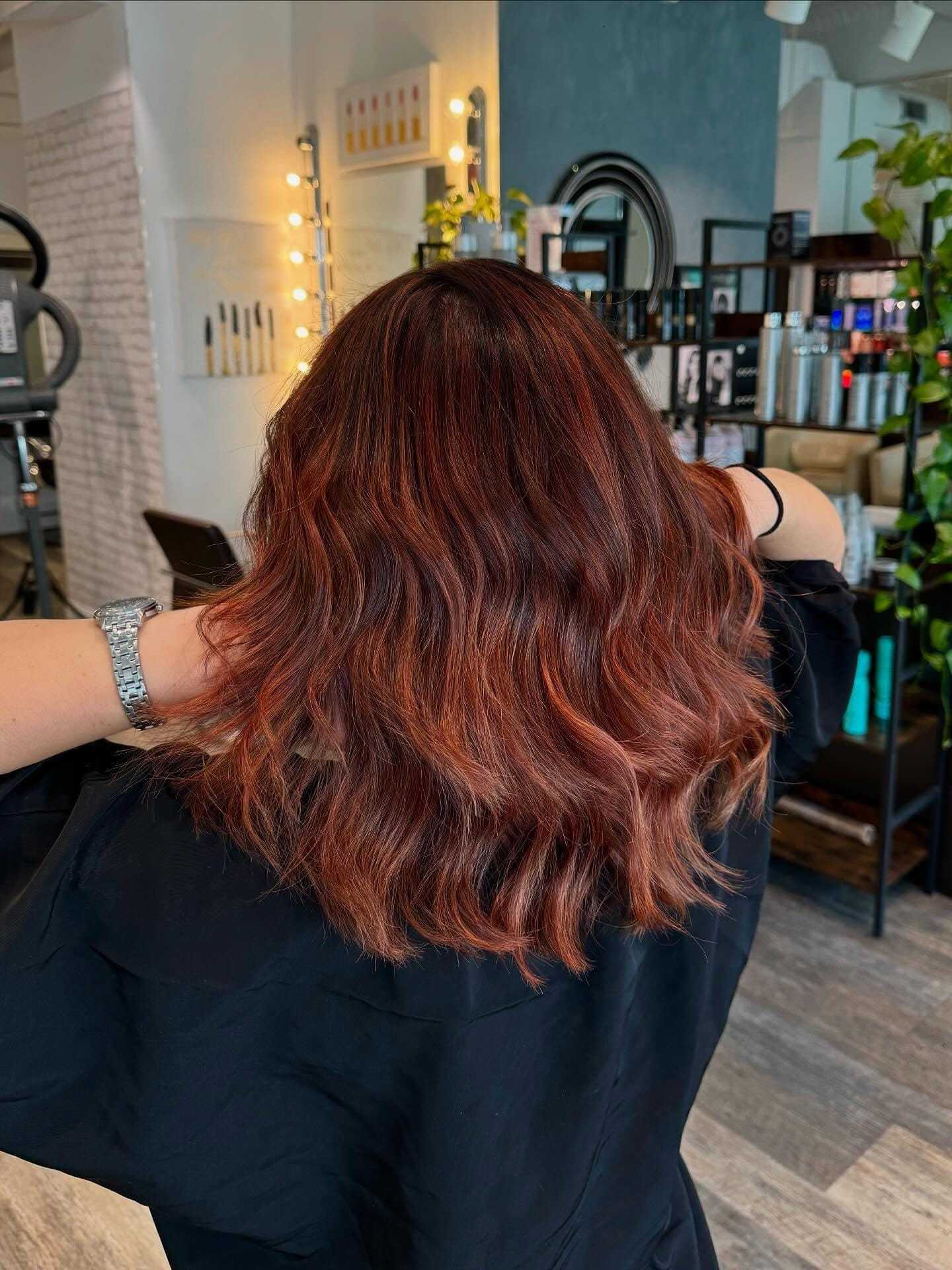 Red-brown wavy hairstyle in a salon, viewed from the back.