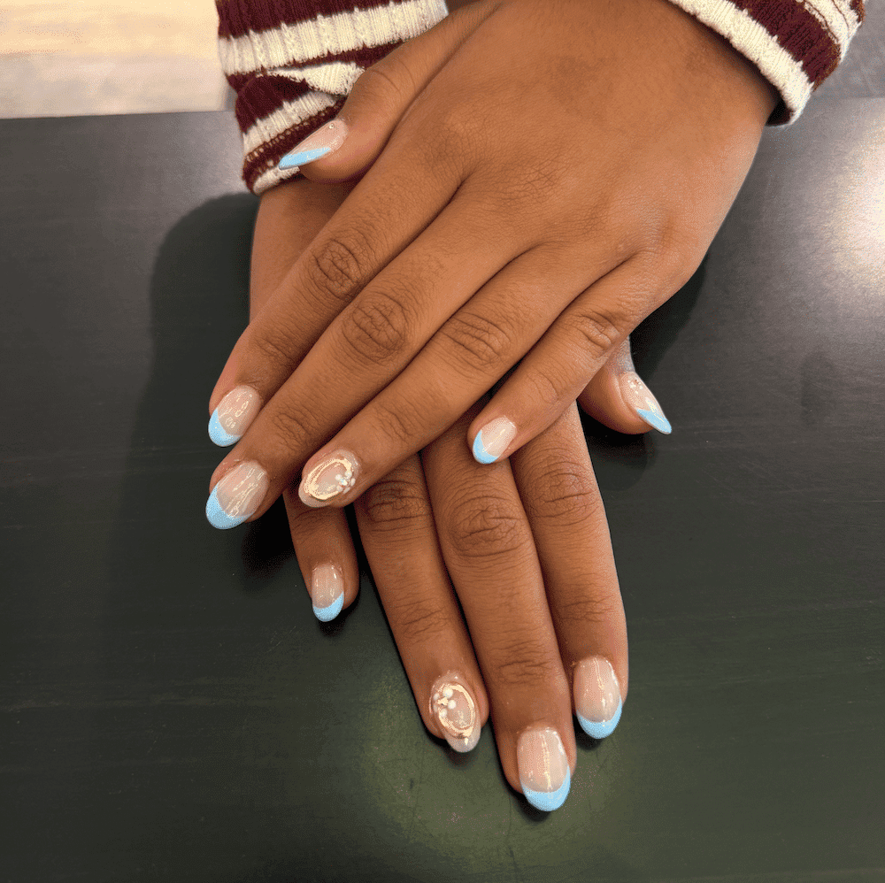 Nails with blue French tips and decorative accents on dark table.