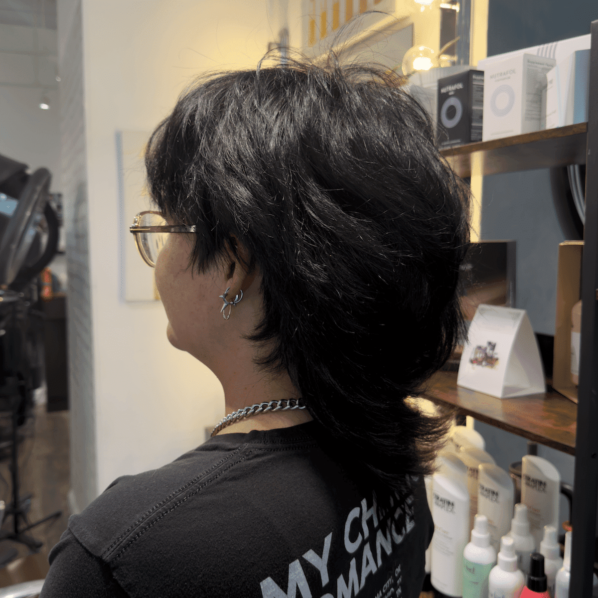 Person with a layered mullet haircut poses in a salon setting.