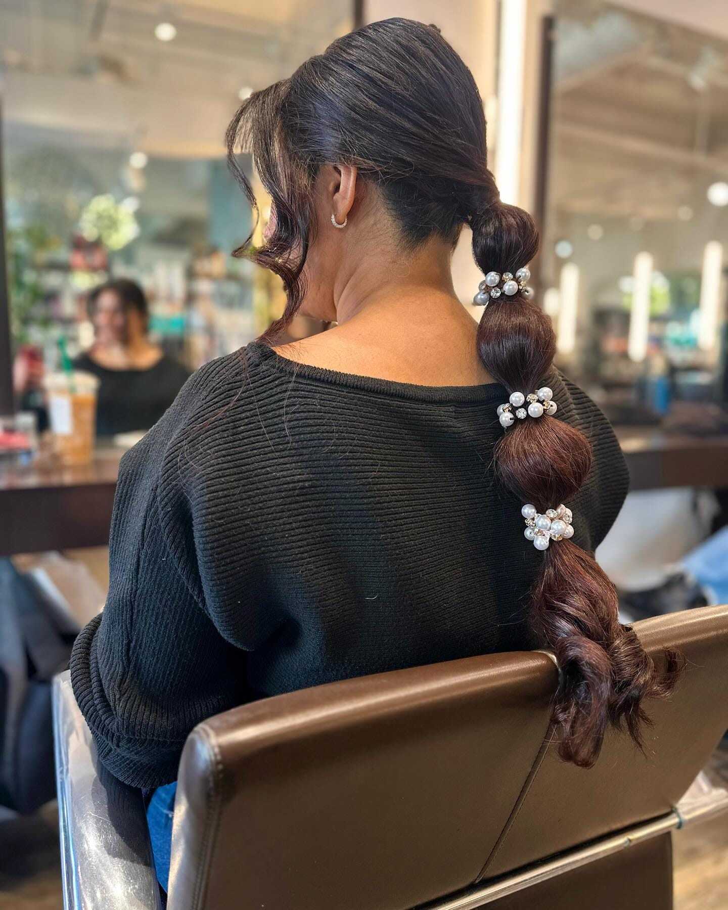 Hair salon customer with stylish braided ponytail, adorned with large silver hair clips.